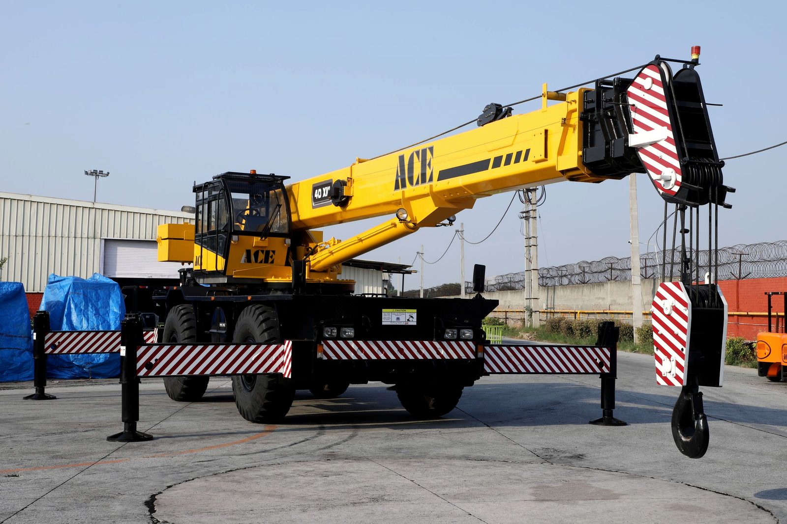 A rough terrain mobile crane with its boom raised in an industrial yard